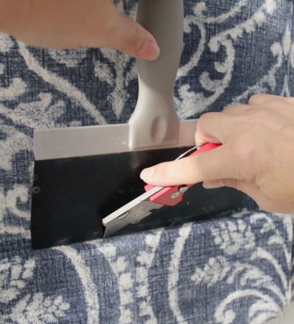 Temporary Wallpaper Tutorial: using a drywall spatula and a razor blade, trim the excess fabric.
