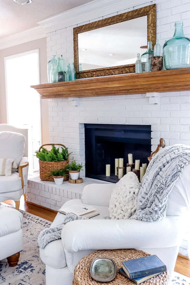 Living room fireplace filled with candles with a mirror over the mantel with blue bottles