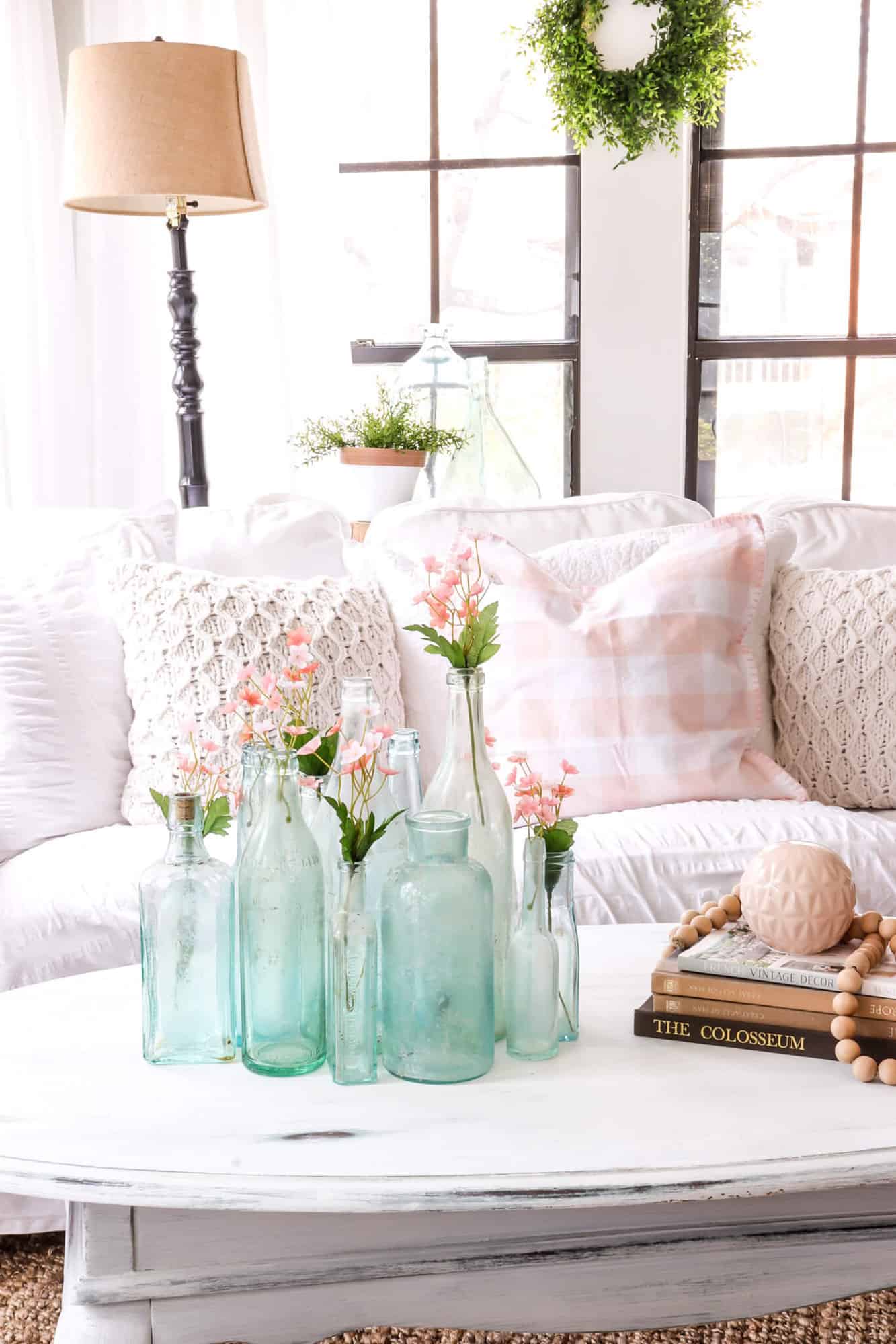 white couch in a sunroom behind a table with vintage blue bottles