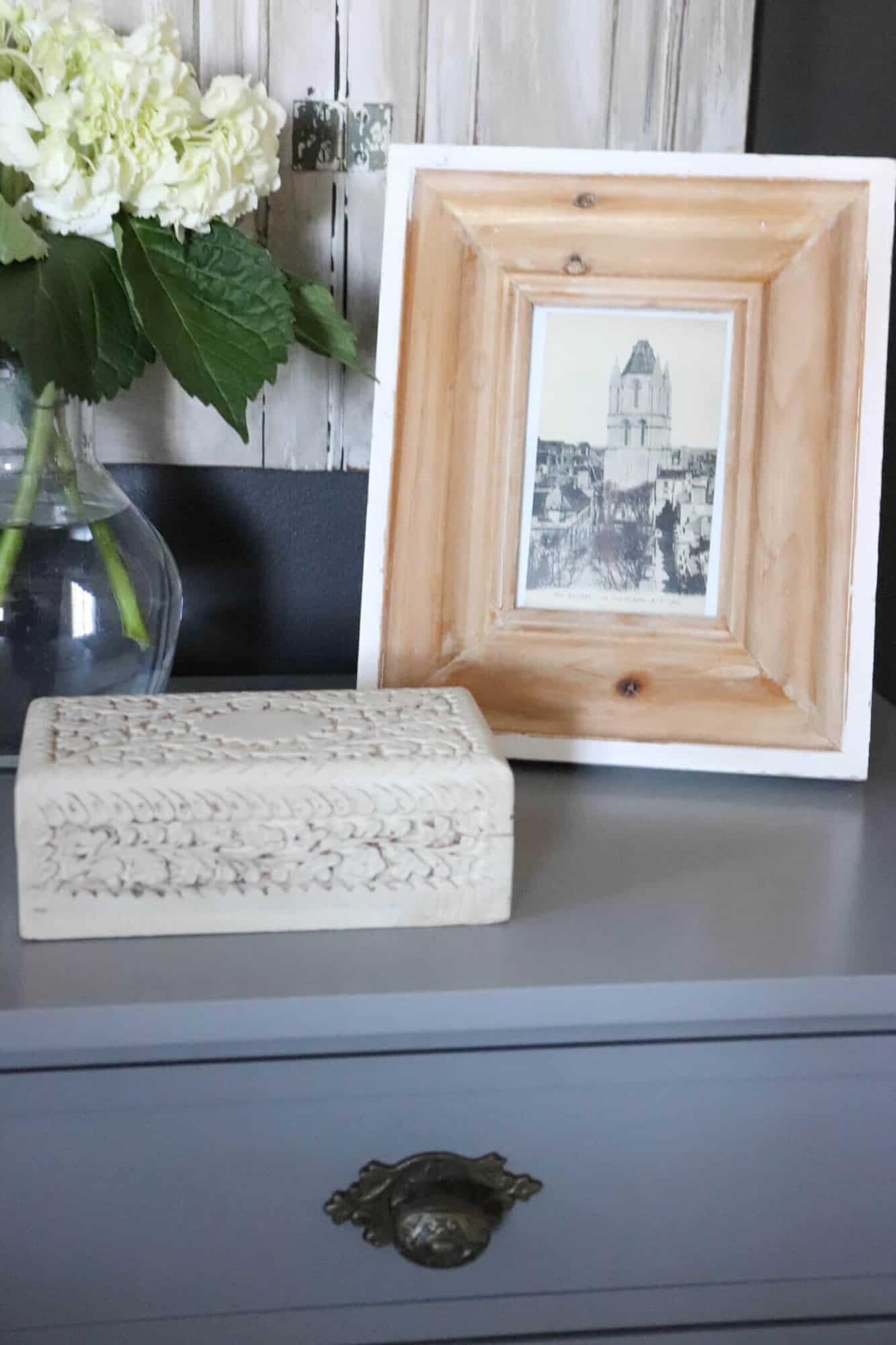 bedside table with hydrangeas and picture frame with vintage postcard