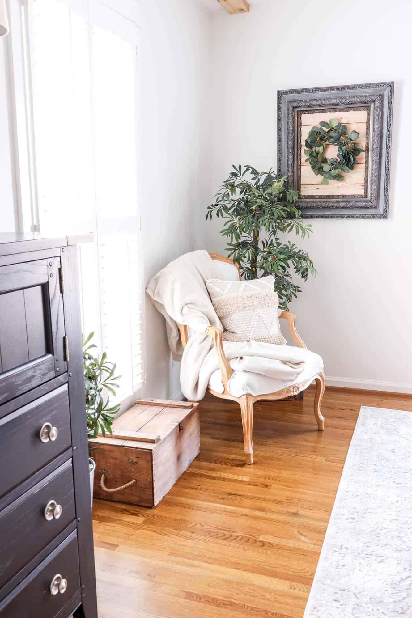 French armchair sitting in bedroom corner with olive tree and framed shiplap wall art