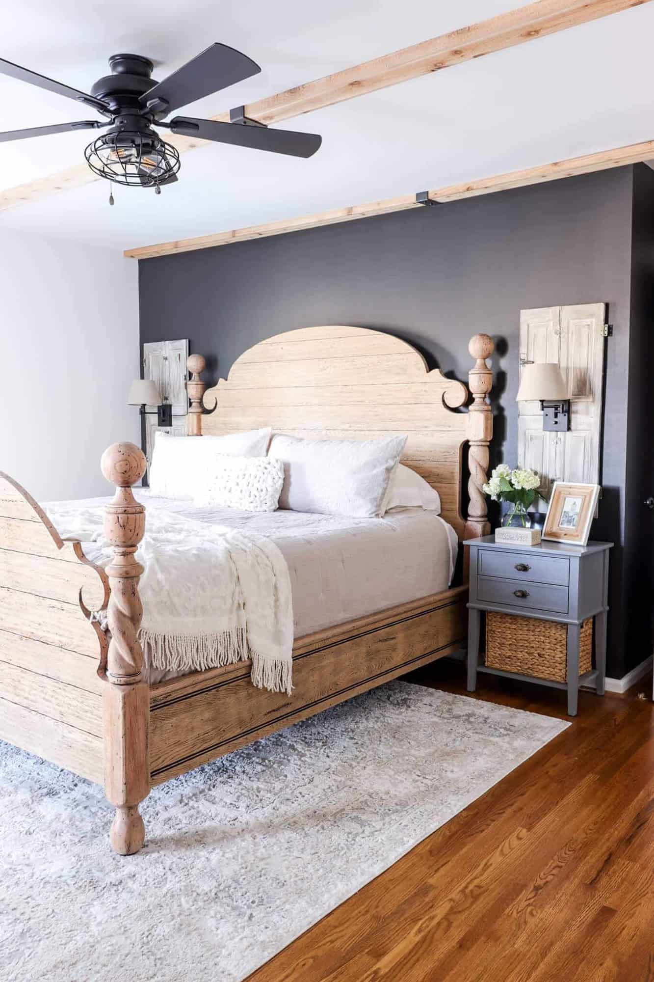 bedroom with large carved bed frame, black accent wall, cedar ceiling beams and shutter side lights