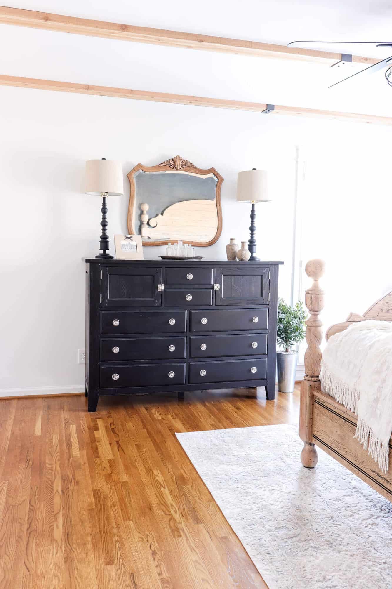 black dresser with vintage mirror against a white wall in a room with cedar beams on the ceiling