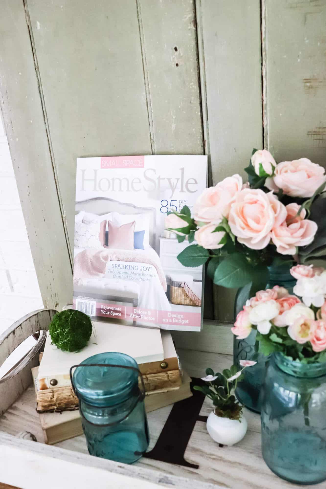 Small Space HomeStyle Magazine next to a tray with unbound books and blue ball jars filled with pink roses