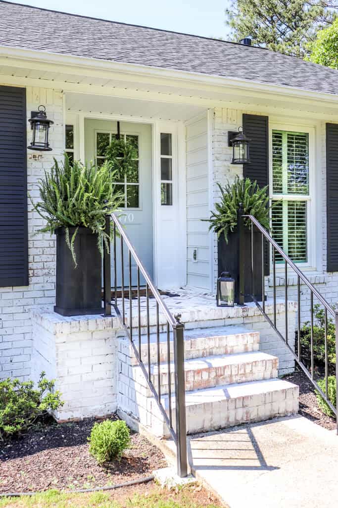 DIY Farmhouse Porch Planter Boxes on a limewashed house with black shutters and black iron handrails