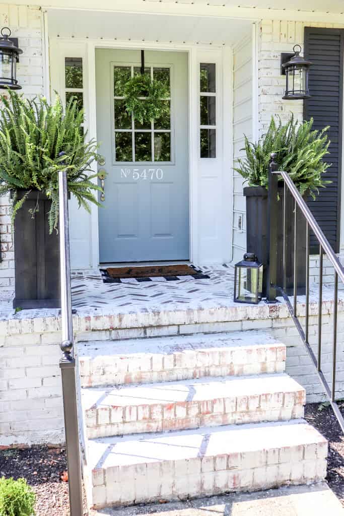 DIY Farmhouse Porch Planter Boxes on a limewashed house with black shutters and black iron handrails