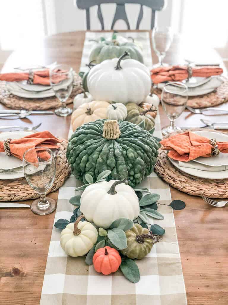 fall dining table with a mixture of faux and real pumpkins on a checkered runner and hyacinth placemats