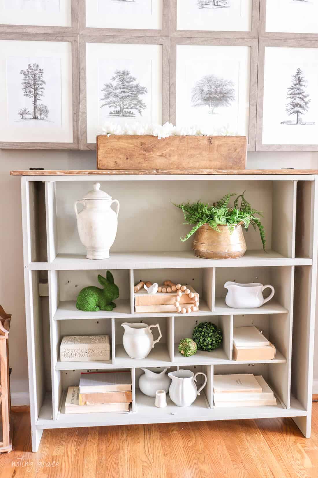 TV cabinet with framed printed artwork. A book case holds vintage books, old creamer pitchers and greenery