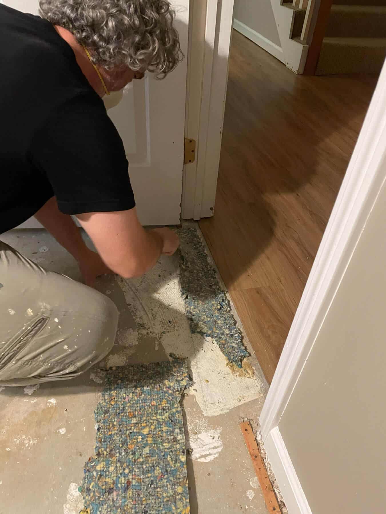 man in black t-shirt scraping carpet glue off concrete basement floor