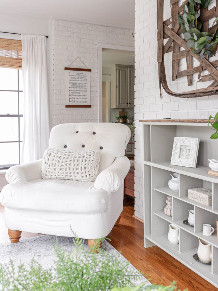 a tufted white armchair next to a bookcase filled with vintage creamer pitchers