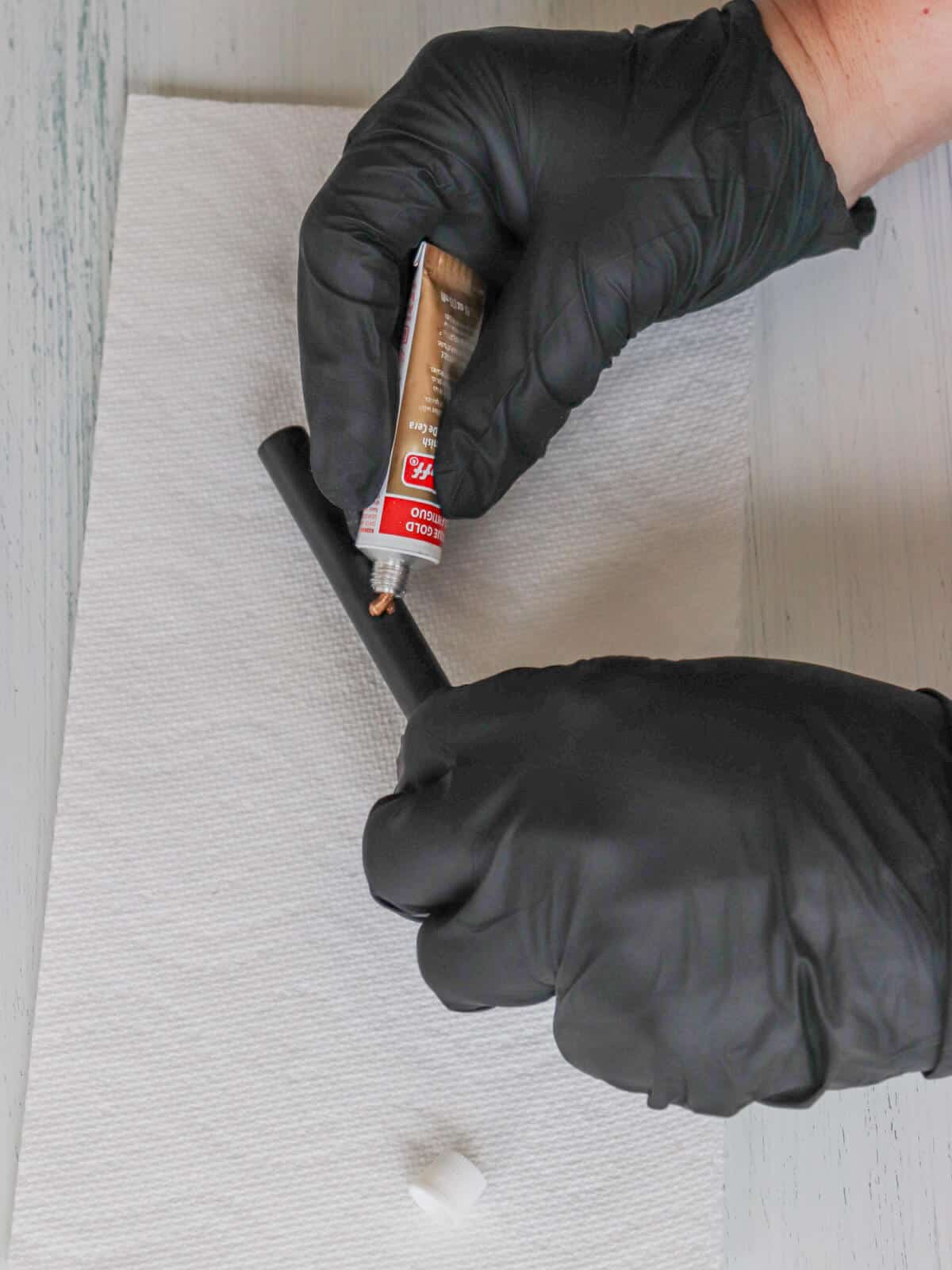 hands wearing black gloves applying antique gold rub n buff to black drawer pulls