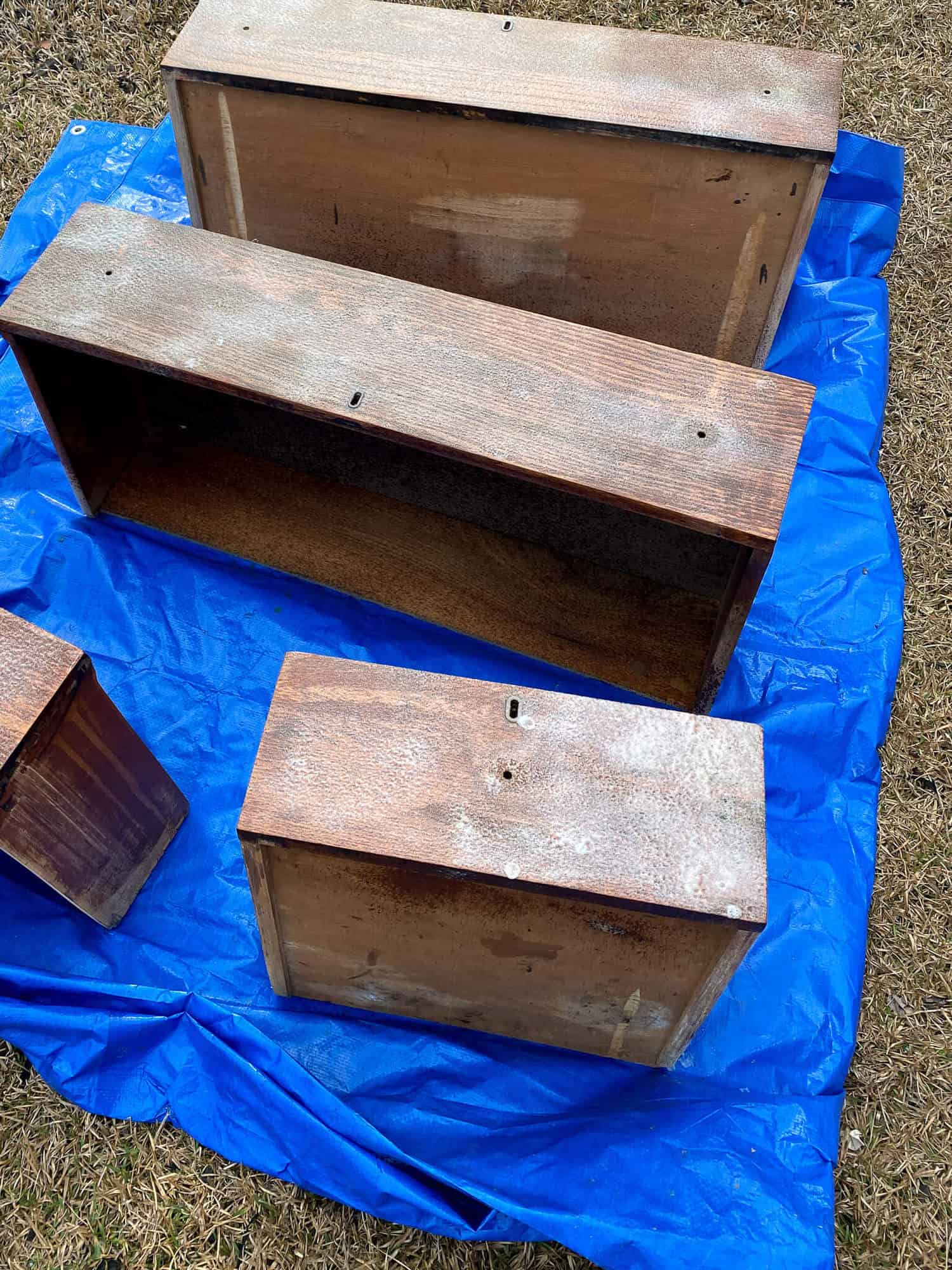 wood drawers on blue outdoor tarp sprayed with oven cleaner to strip finish