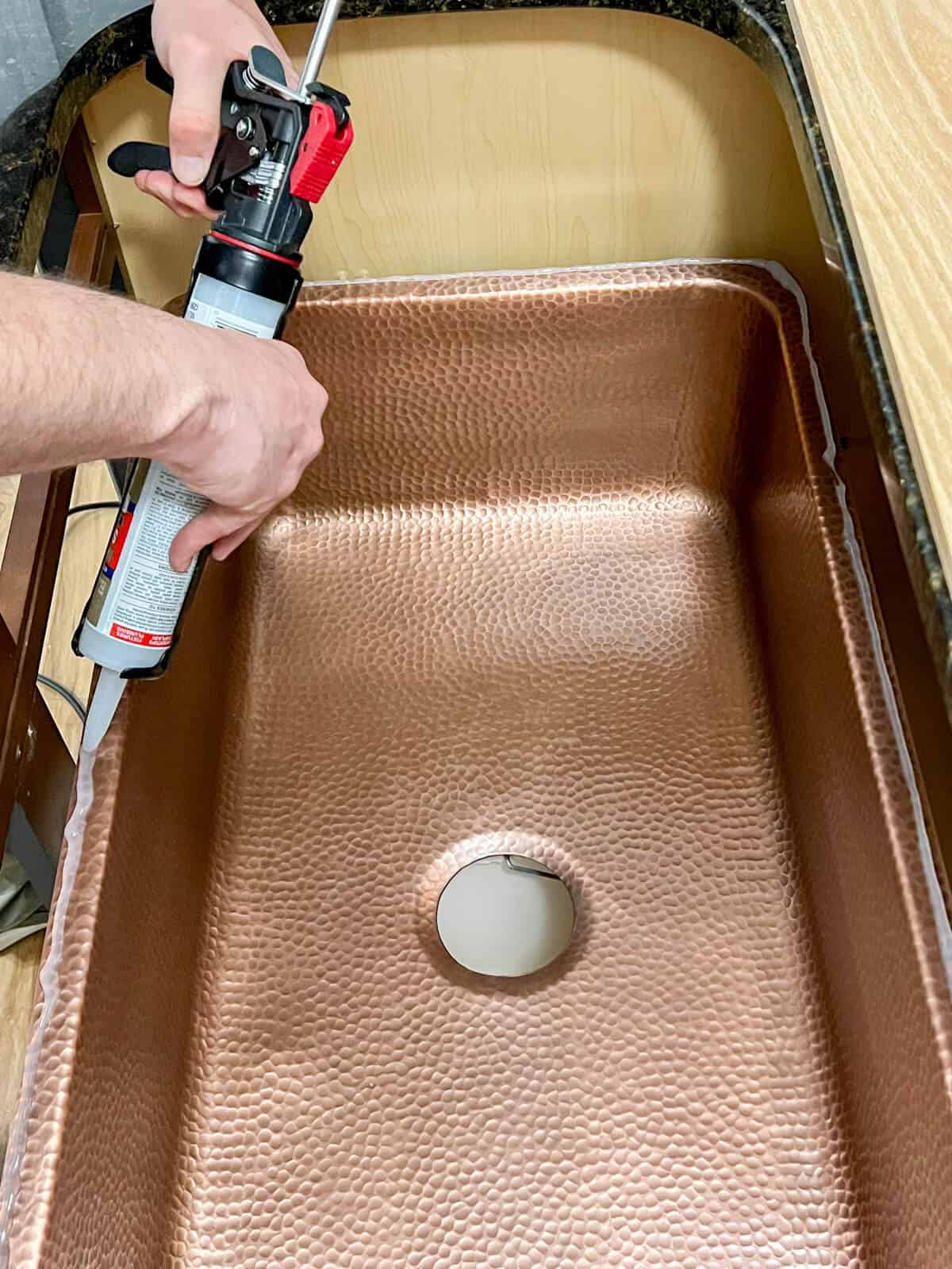 applying silicone adhesive to a hammered copper sink before installation.