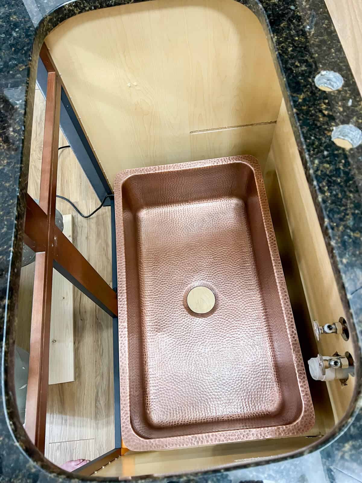 granite kitchen countertop with sink opening cut with a new undermount hammered copper sink getting ready for the install.