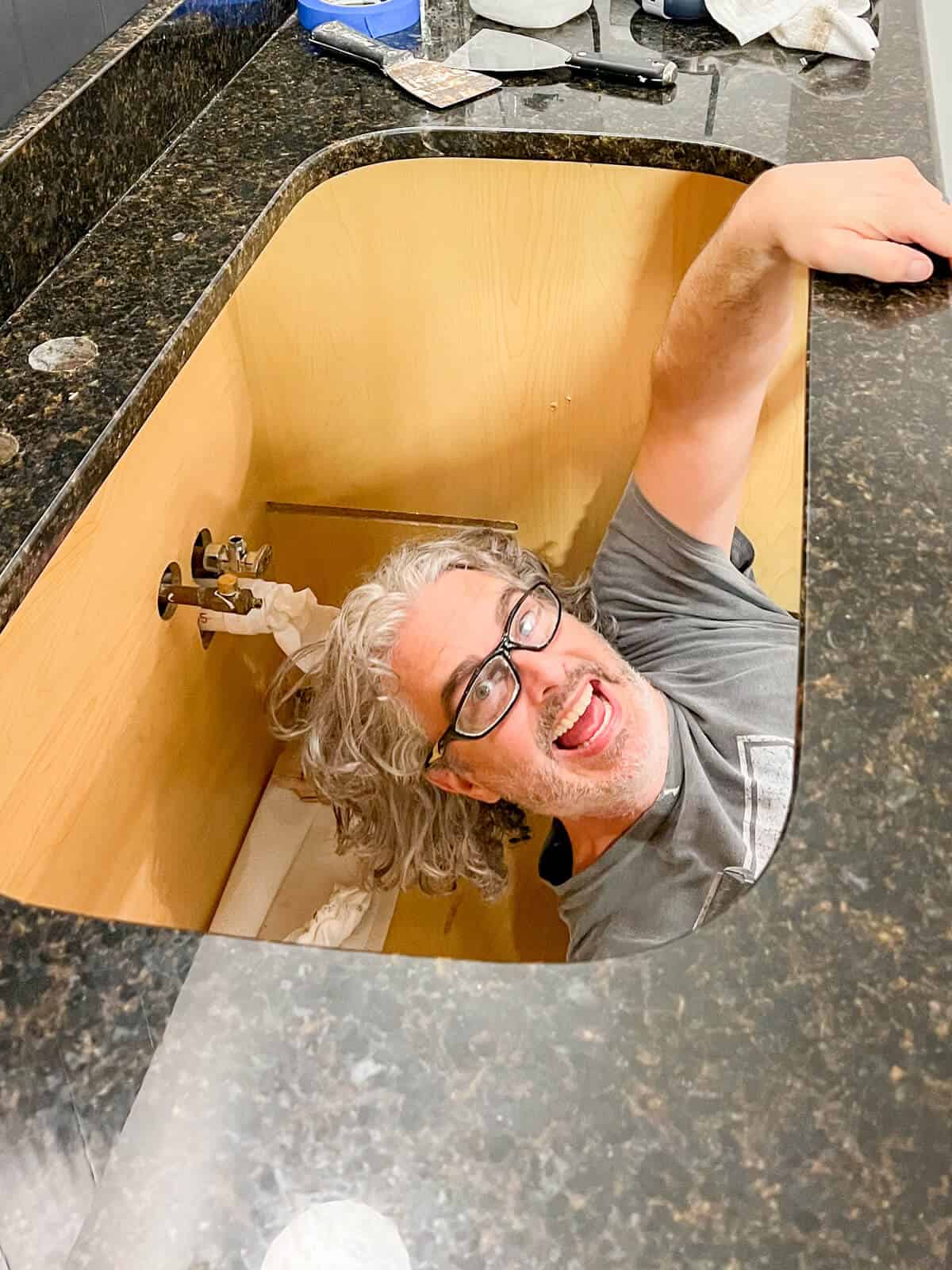man smiling through hole in kitchen counter where a kitchen sink should go