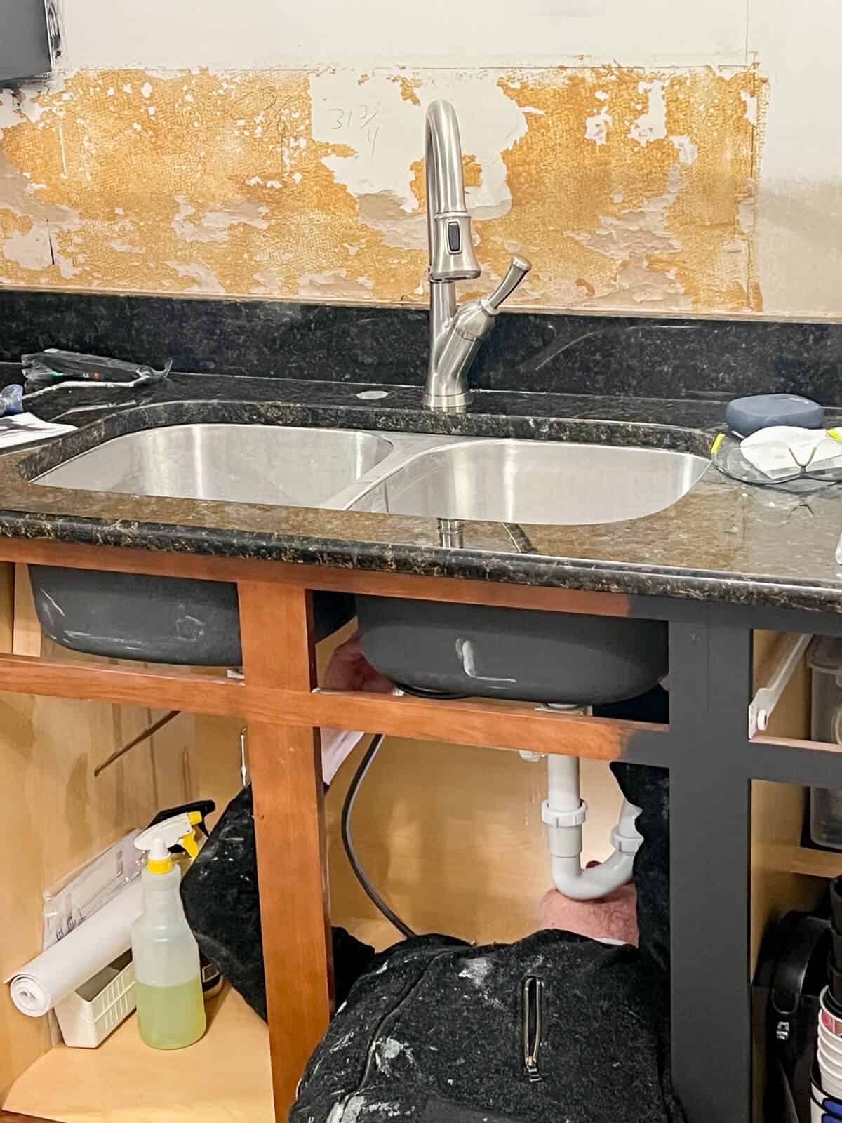 Man looking under a kitchen sink cabinet to begin disconnecting plumbing