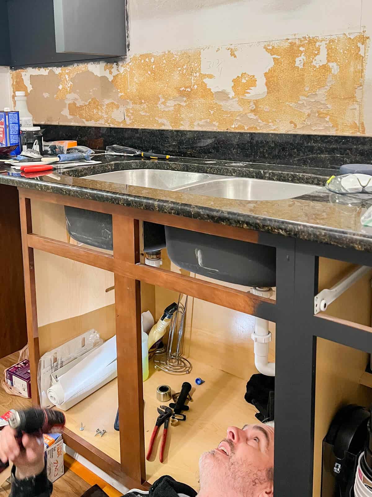 Man looking under a kitchen sink cabinet to see how the undermount sink is attached