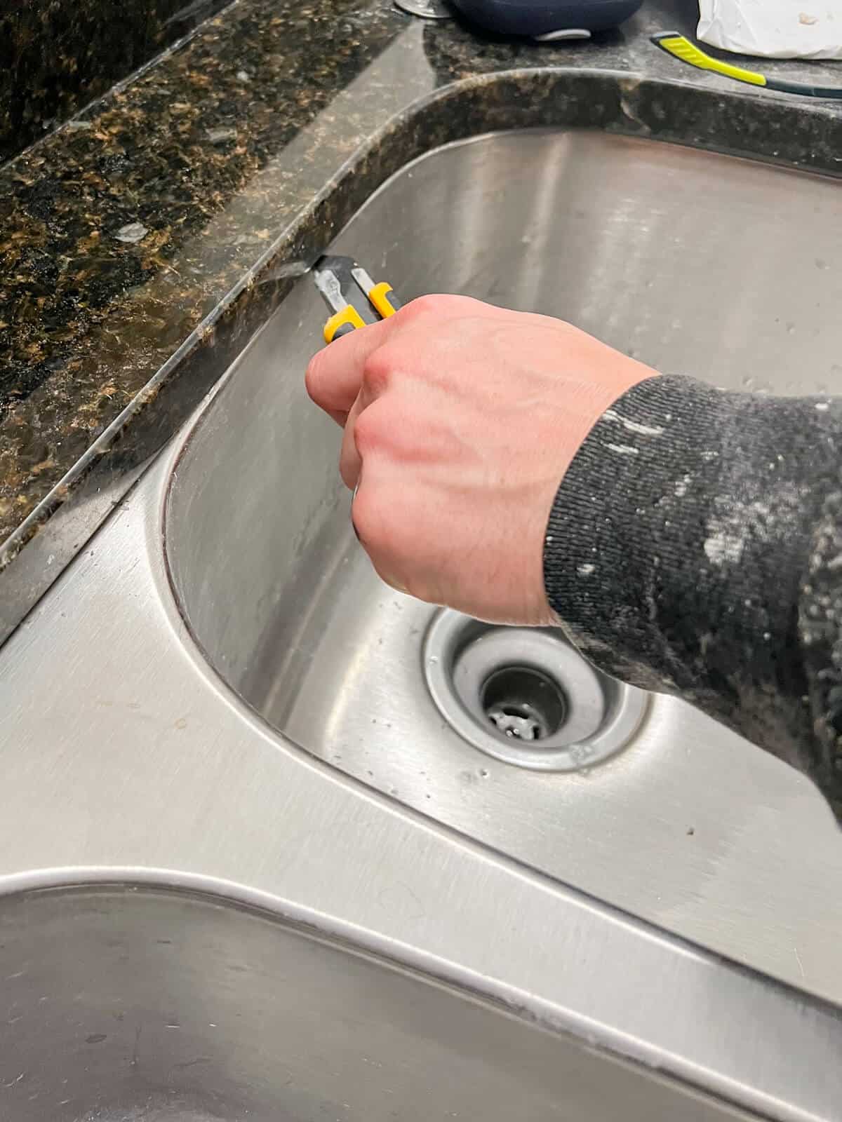 cutting away silicone from a stainless steel undermount sink for removal