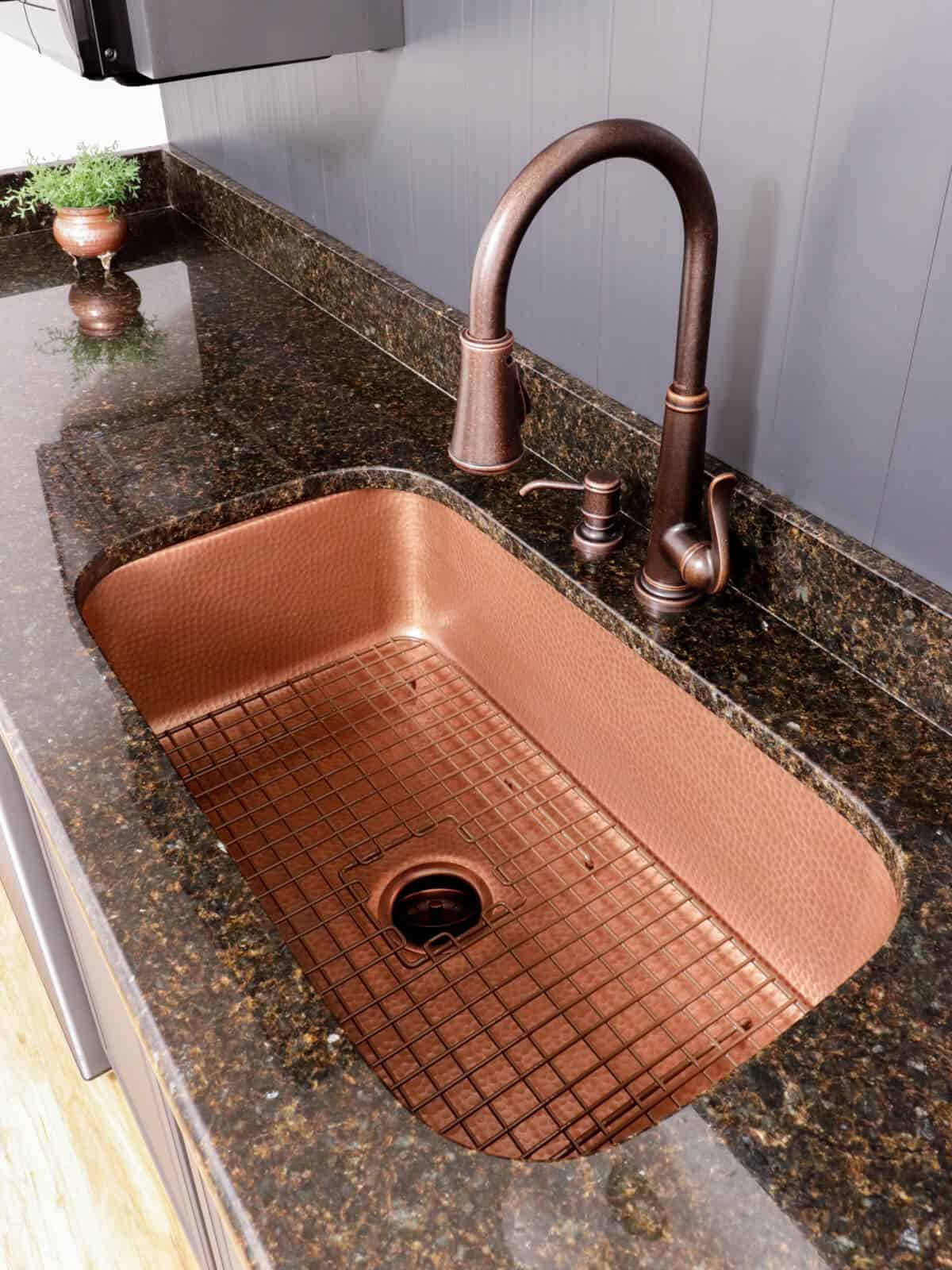 Sinkology copper sink and copper Pfister faucet installed in a dark granite countertop