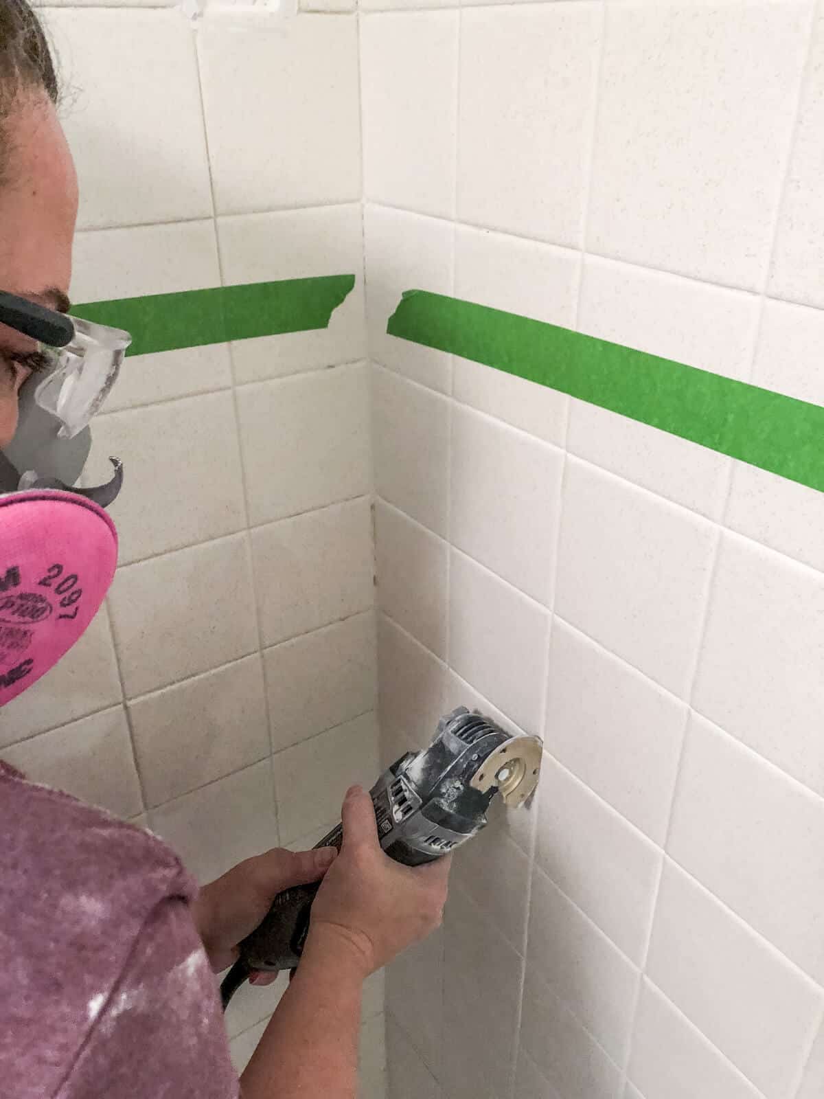 Woman wearing mask and goggles grinding away old grout with a dremel multi max tool
