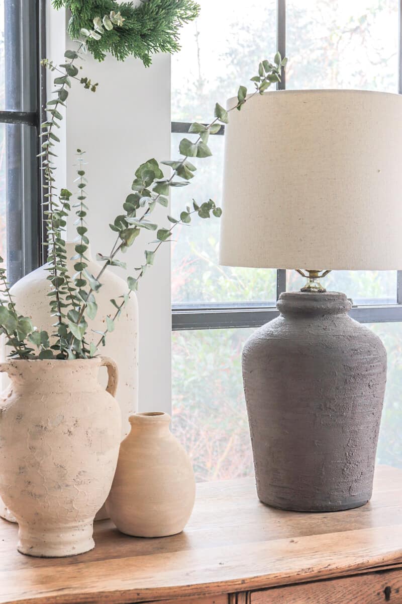 Ceramic urn knock off lamp sitting in front of a window with other textured vases filled with eucalyptus
