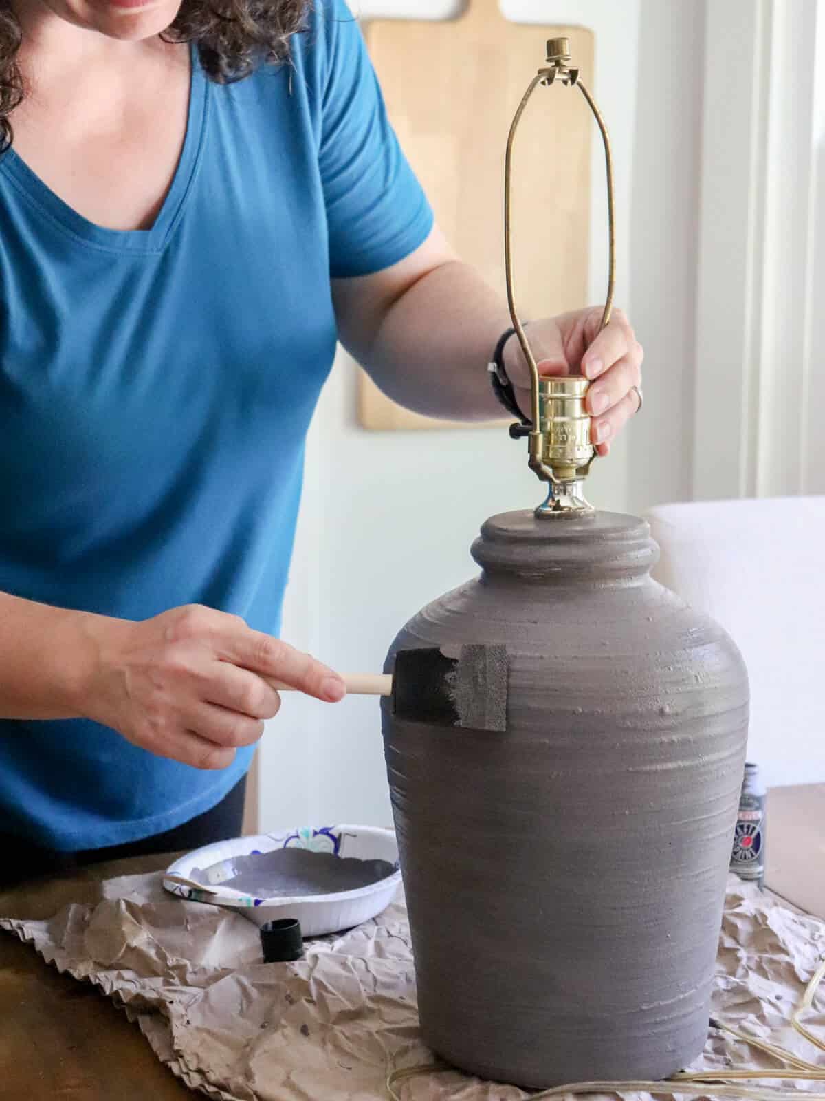 woman painting a lamp with gray baking soda paint with a foam brush