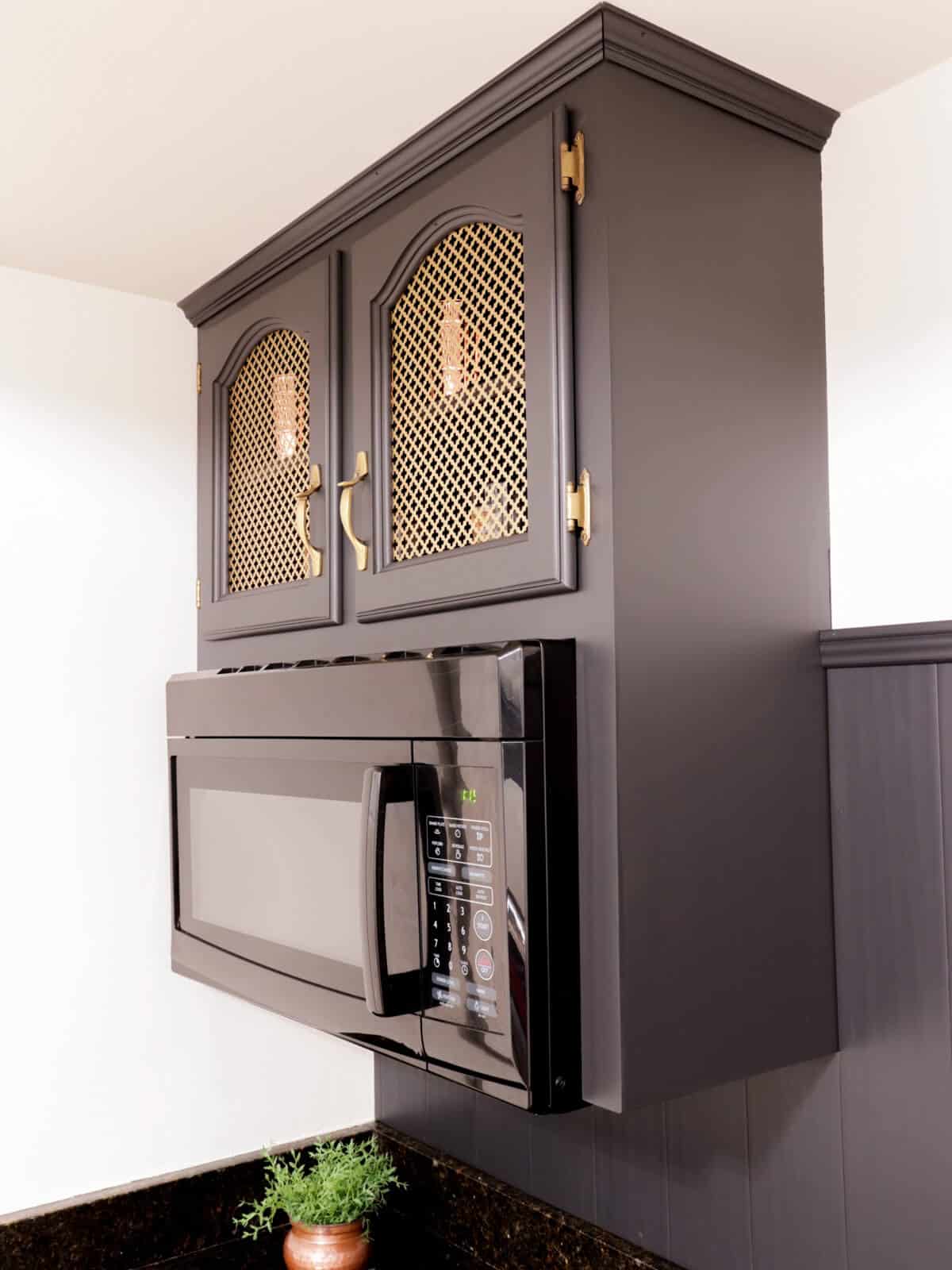old cabinets updated with brass insert above a microwave range hood