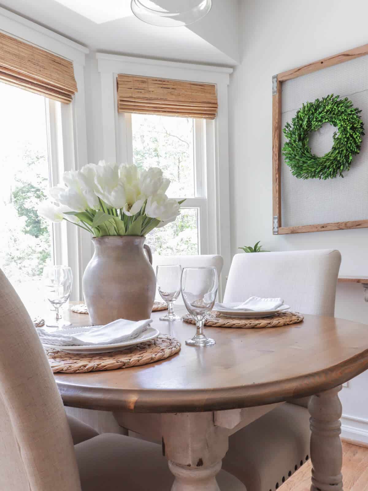 simple tablesetting with woven placemats, white plates and napkins and a pottery pitcher filled with faux tulips