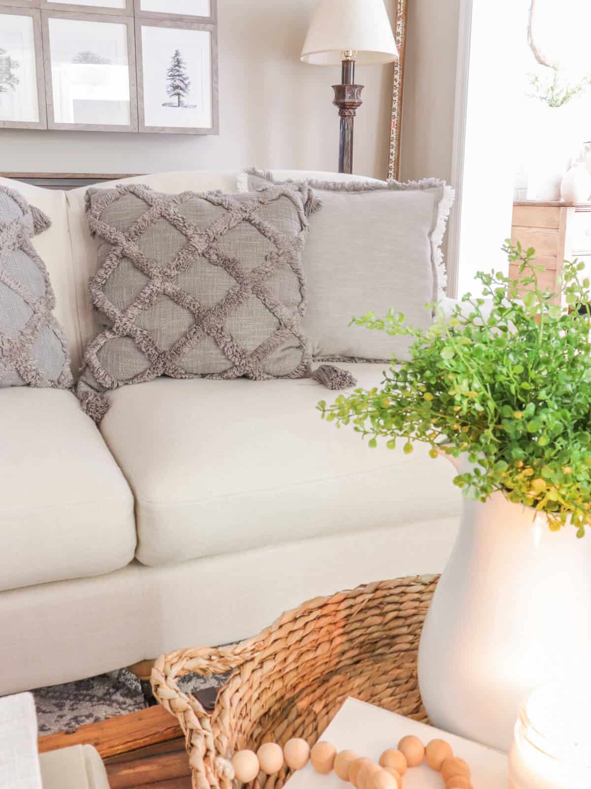 cream sofa with gray pillows with a coffee table in front holding a woven tray and white vase filled with greenery