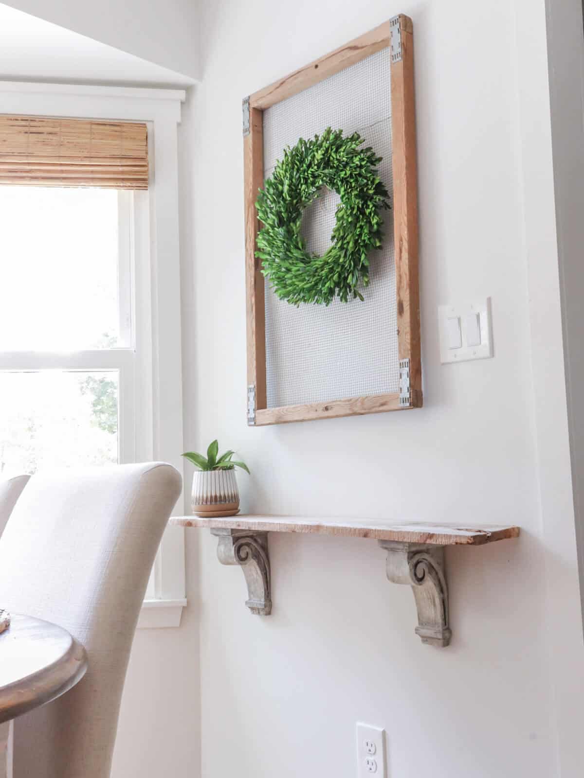 wood framed screening with a wreath hanging over a small wall shelf