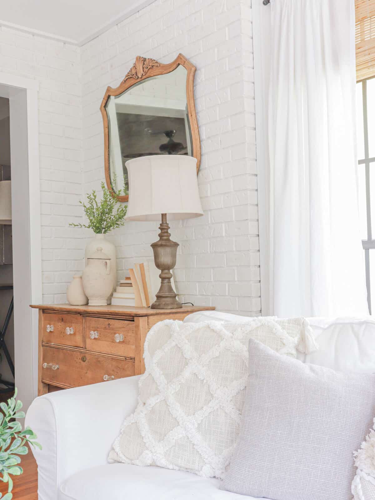 White brick walls with unfinished wood furniture behind a white slipcovered couch with better homes and gardens trellis pillows