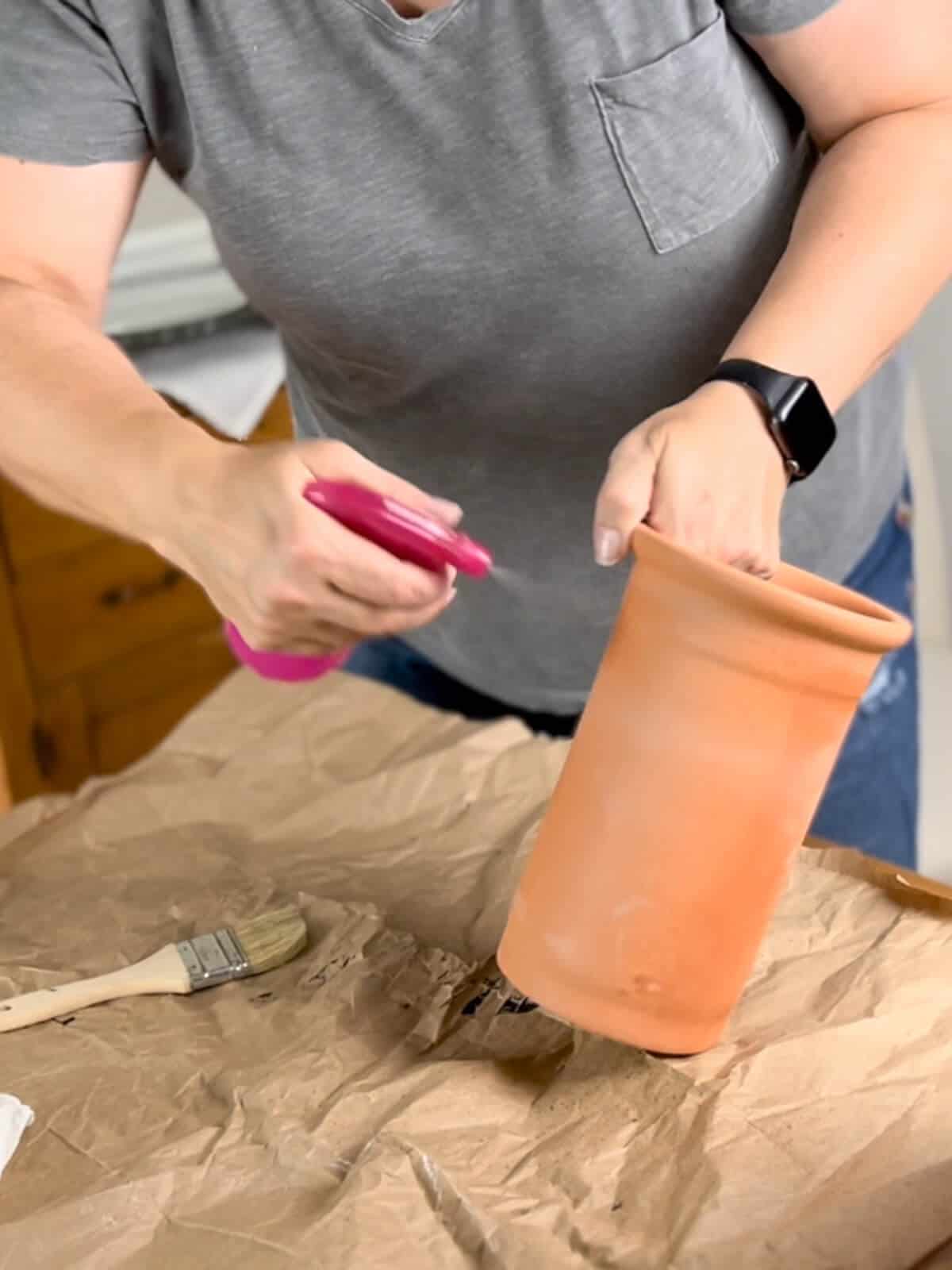 spraying a terracotta flower vase with water