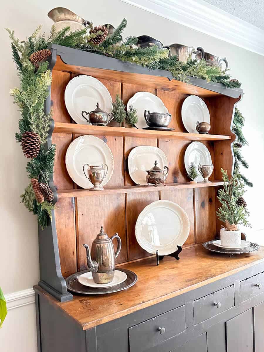 vintage hutch decorated with tarnished silver and ironstone plates and winter garland