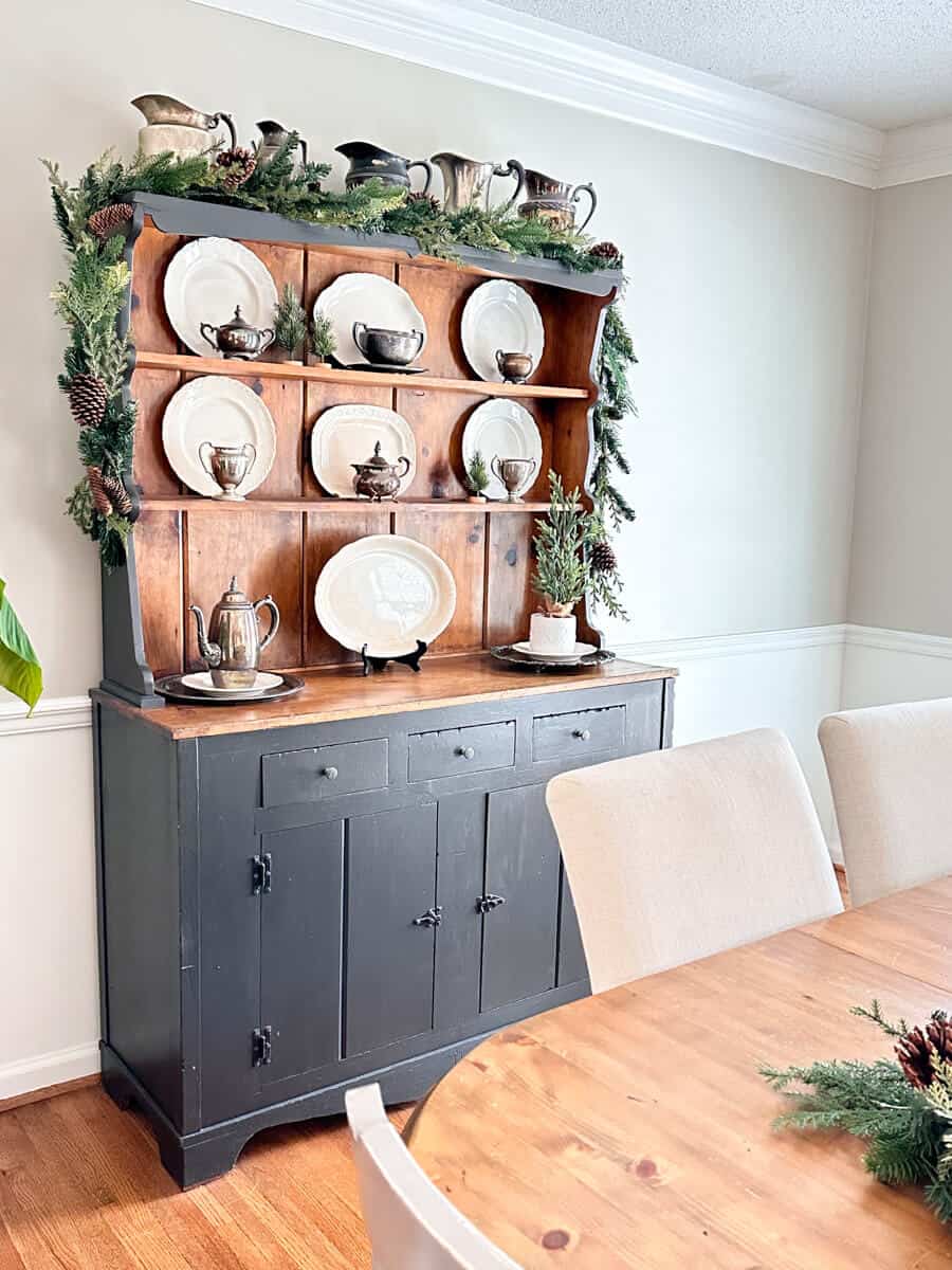 dining room with garland decorated hutch filled with vintage plates and silver