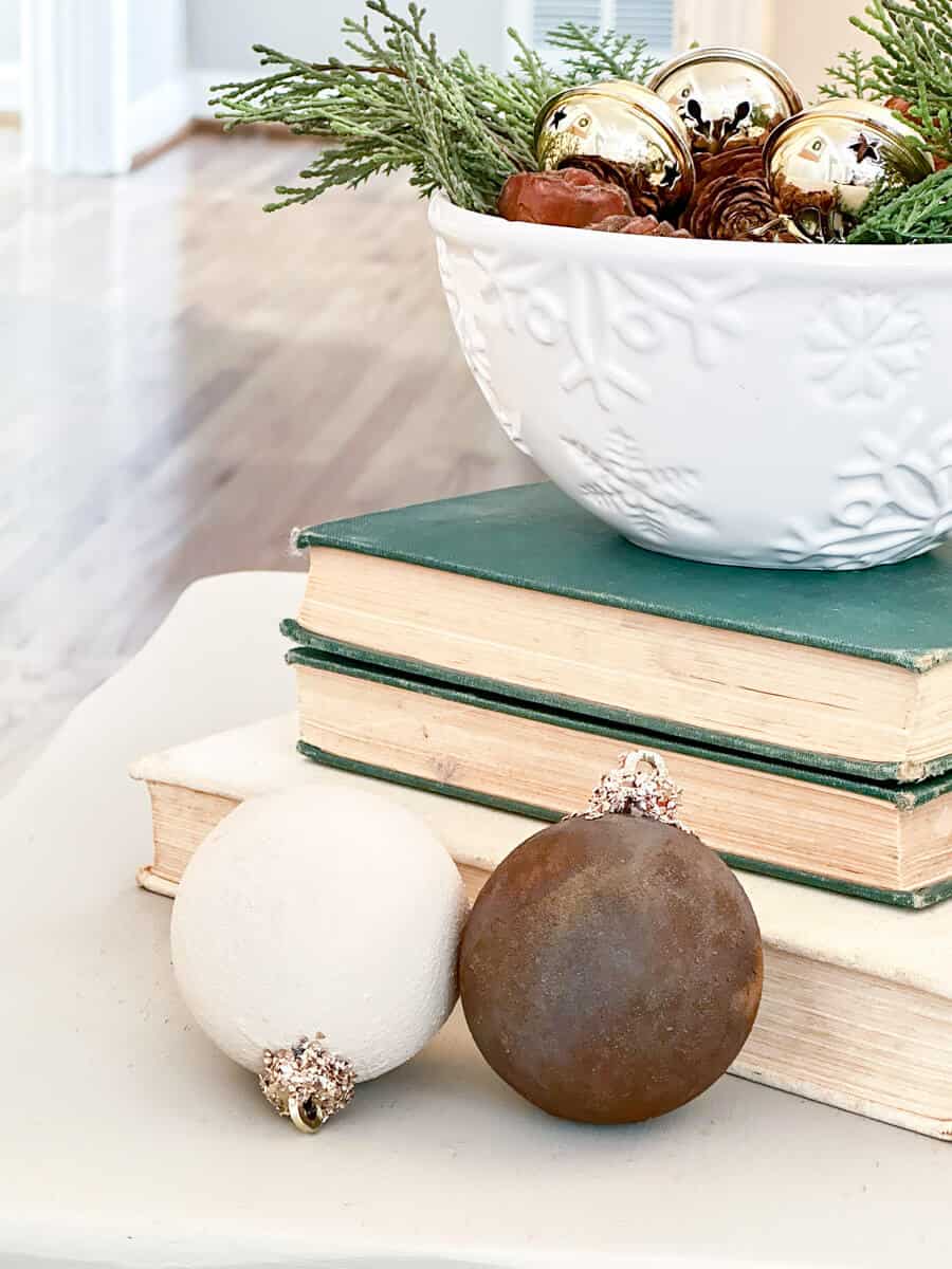 snowflake dish filled with greenery and bells sitting on books next to 2 ornaments