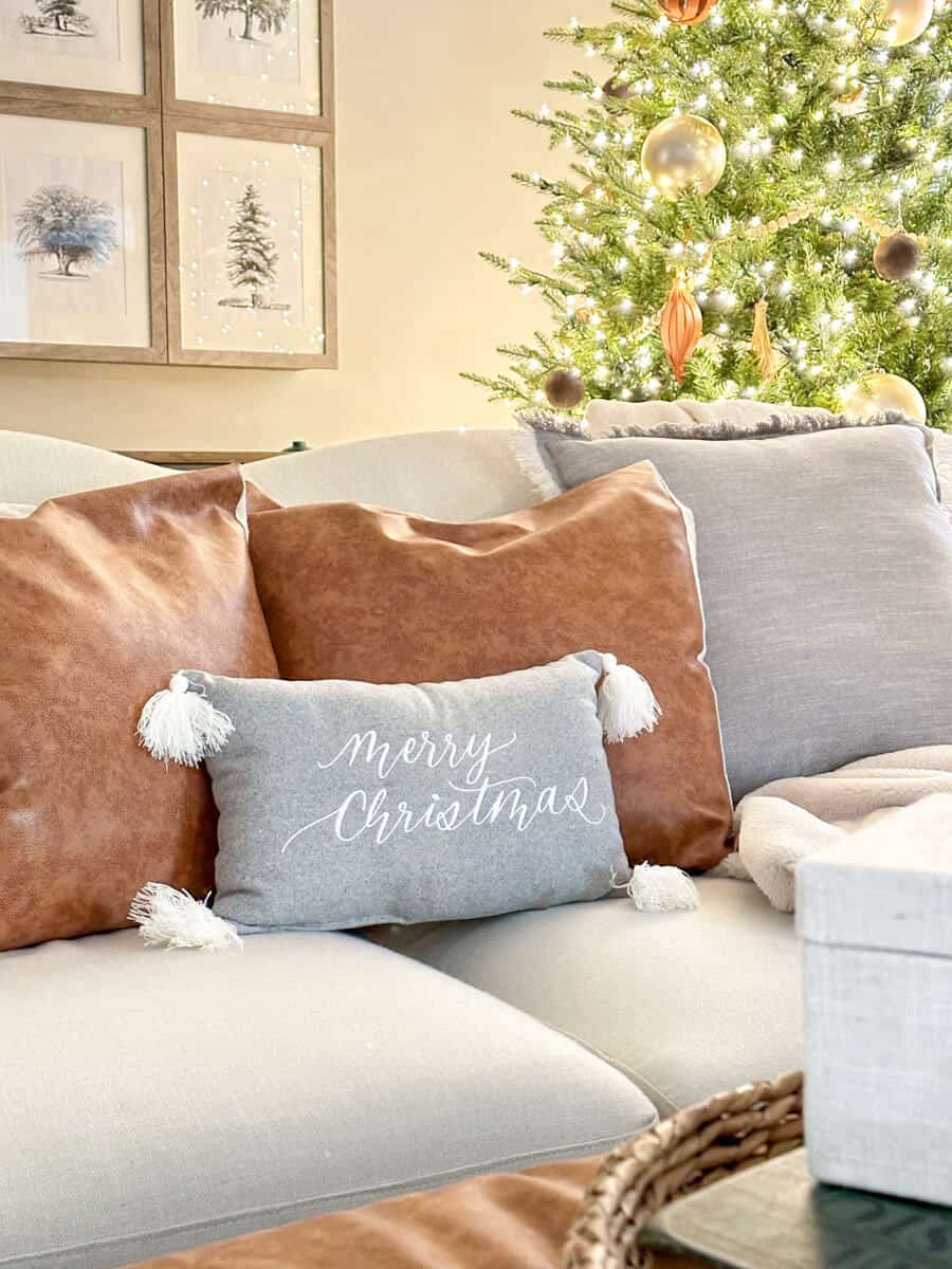 tan couch with gray and camel leather pillows and a soft merry Christmas pillow