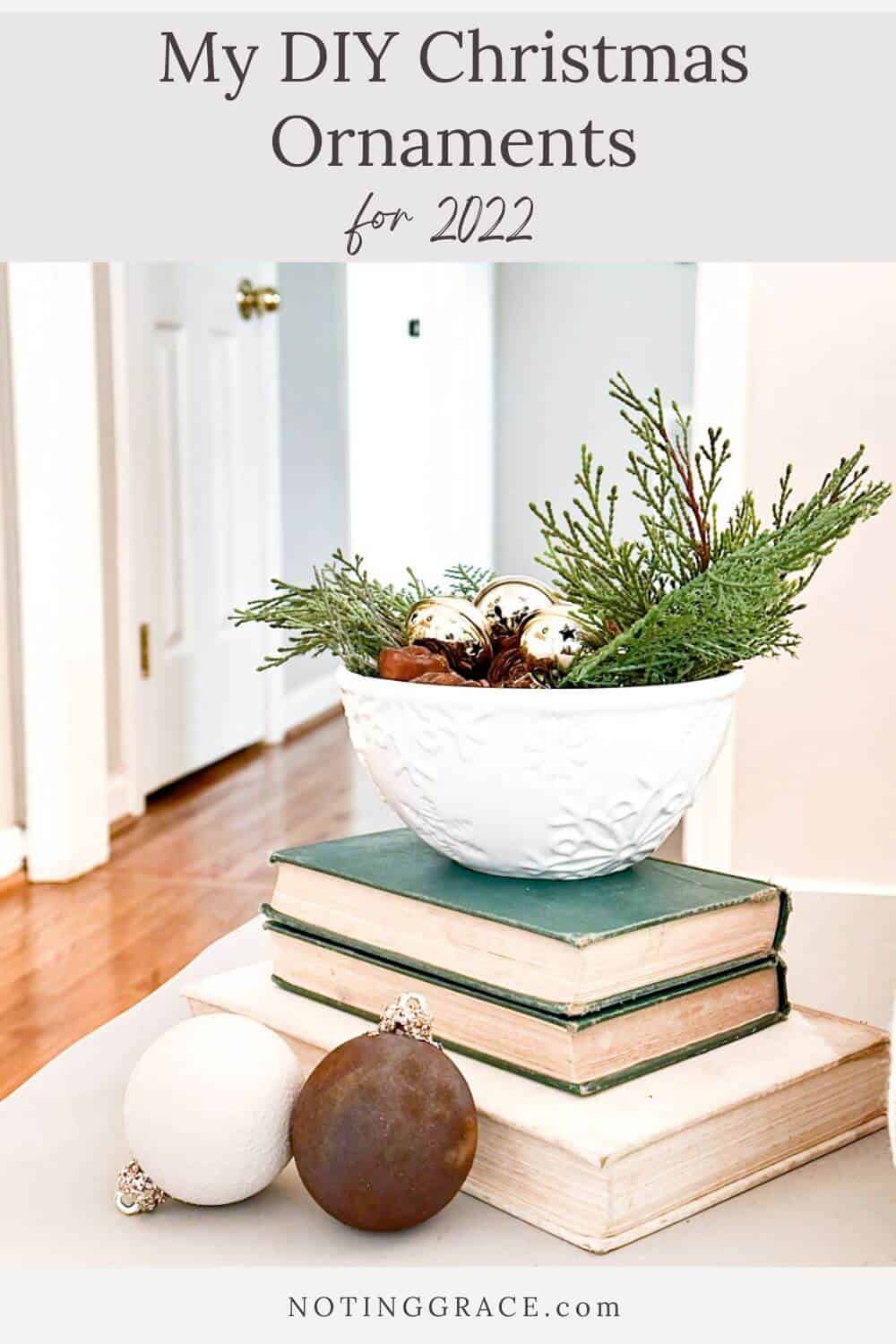 snowflake dish filled with greenery and bells sitting on books next to 2 ornaments