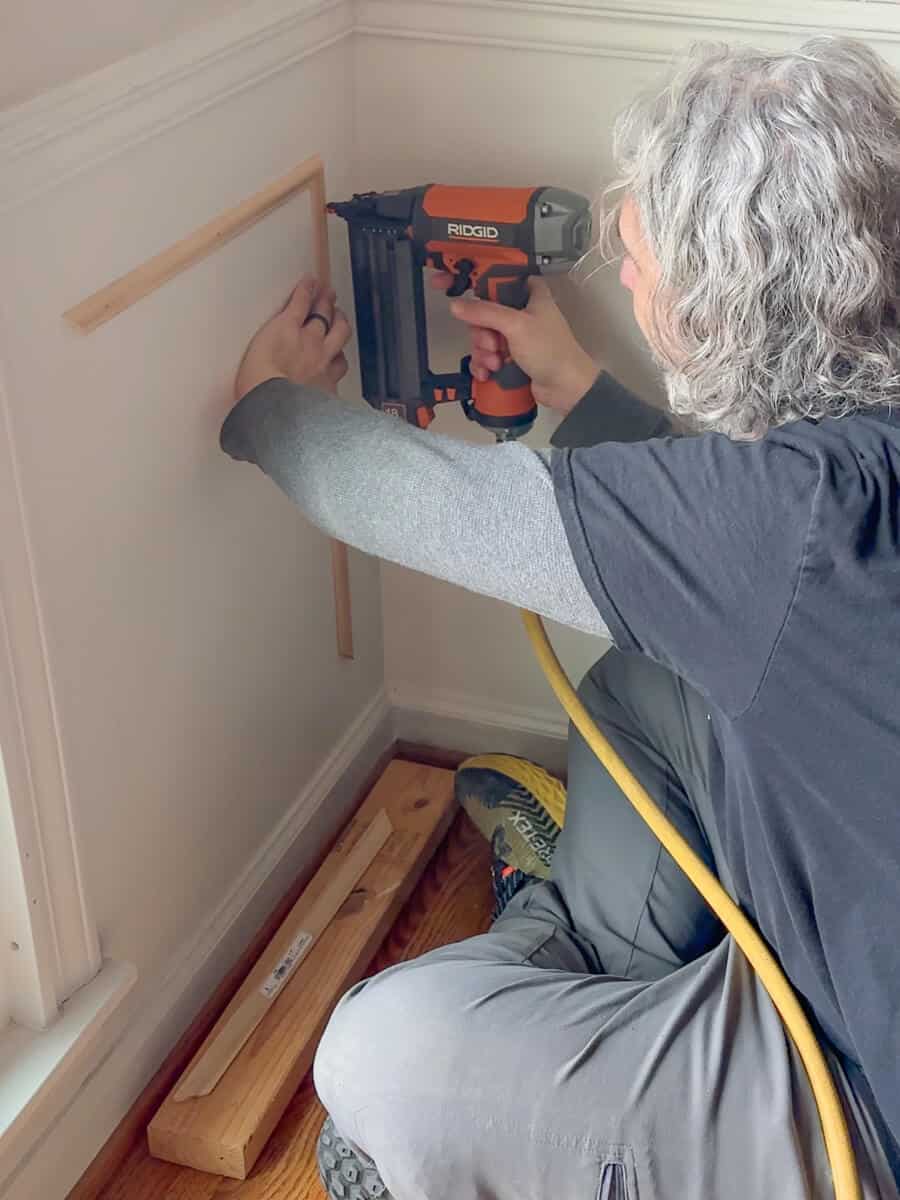 Man installing Picture Trim Molding under chair rail molding with a pneumatic nail gun