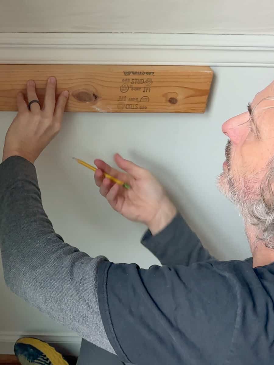 Man installing Picture Trim Molding under chair rail molding using a 2 x 4 to mark the measurements