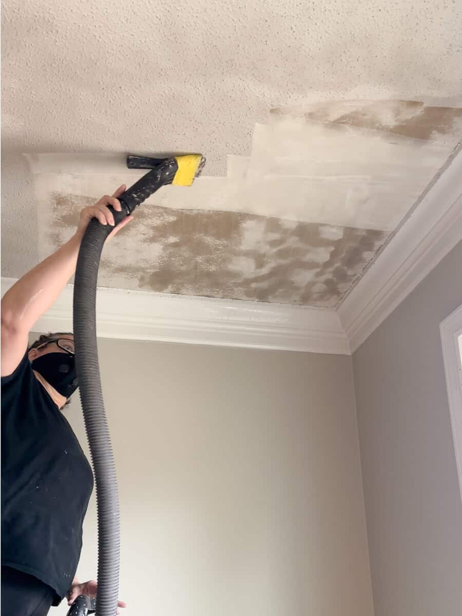woman scraping popcorn ceiling using a shop vac with a putty knife taped to the end