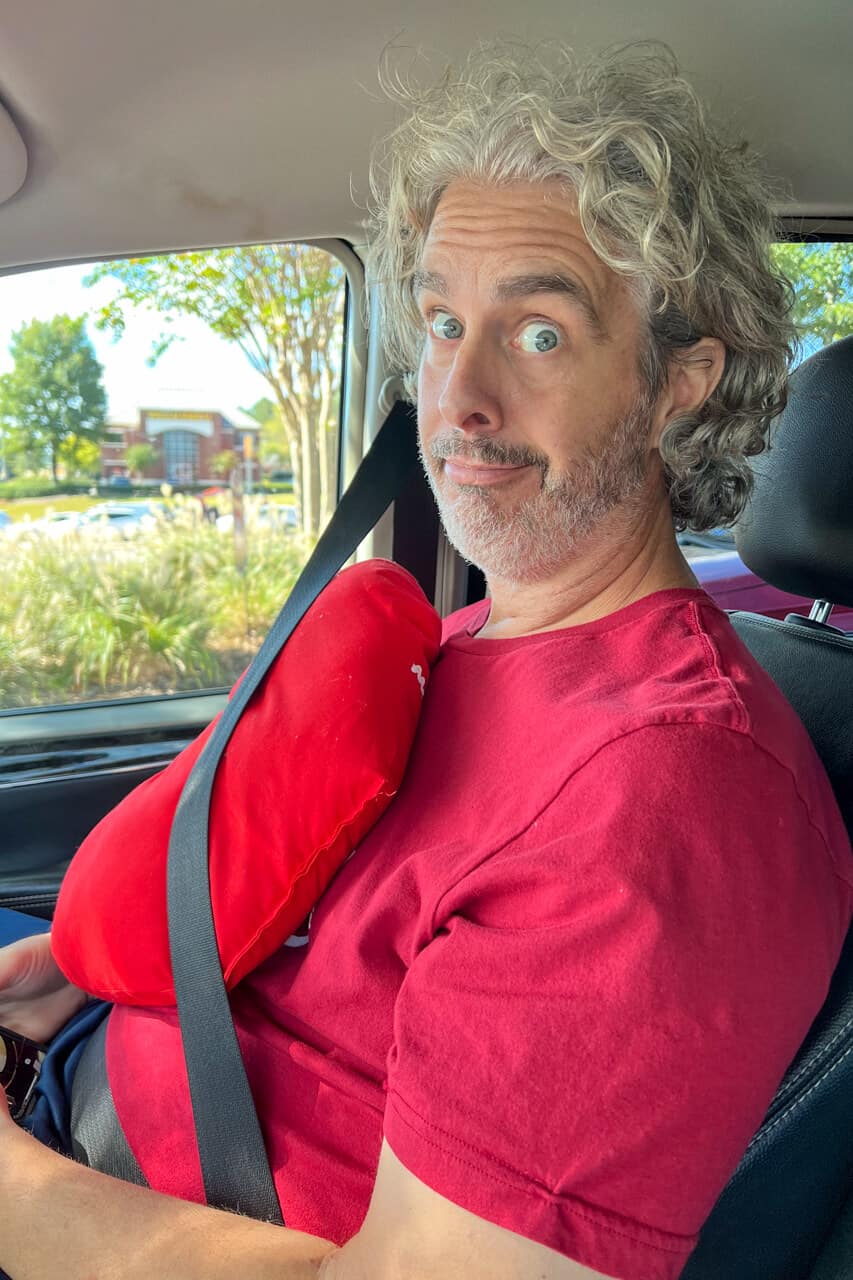 man sitting in a car with a pillow placed between his chest and the seatbelt