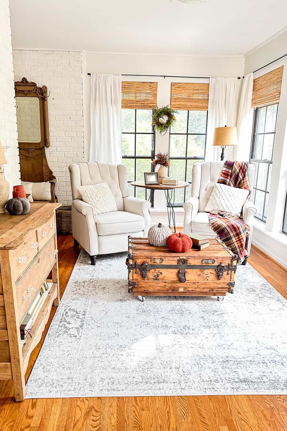 Pair of wingback armchairs in front of black windows and and old trunk for a coffee table decorated with minimal fall decor