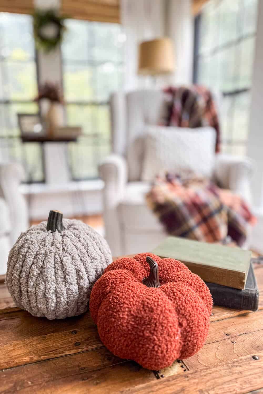 yarn covered pumpkins in front of a wingback armchair with plaid blanket and knit pillow