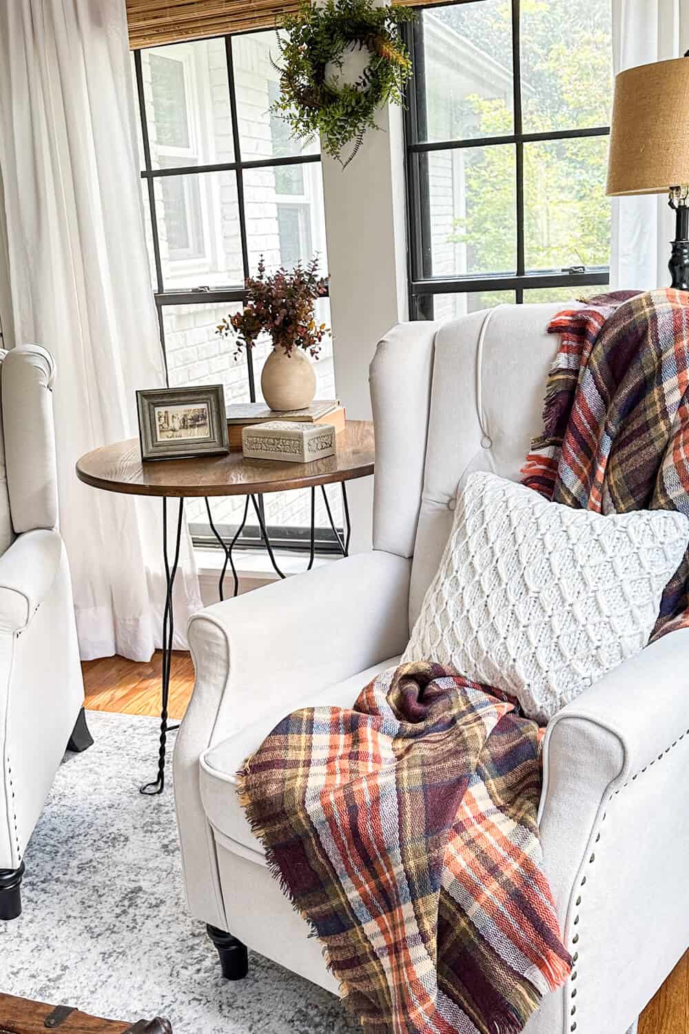 wingback armchair in front of black windows decorated with knit pillowcase and fall plaid throw blanket