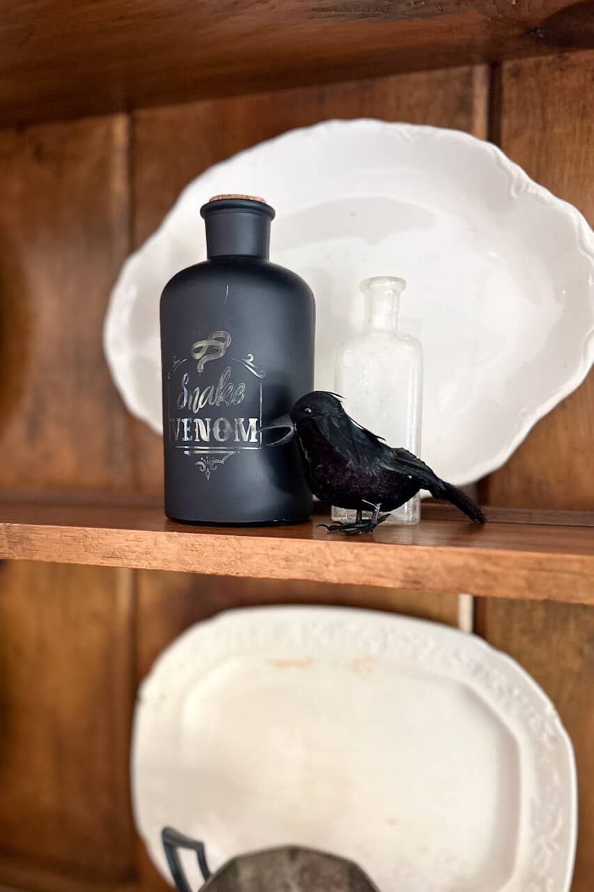vintage dining hutch styled for halloween with bottles and fake crow