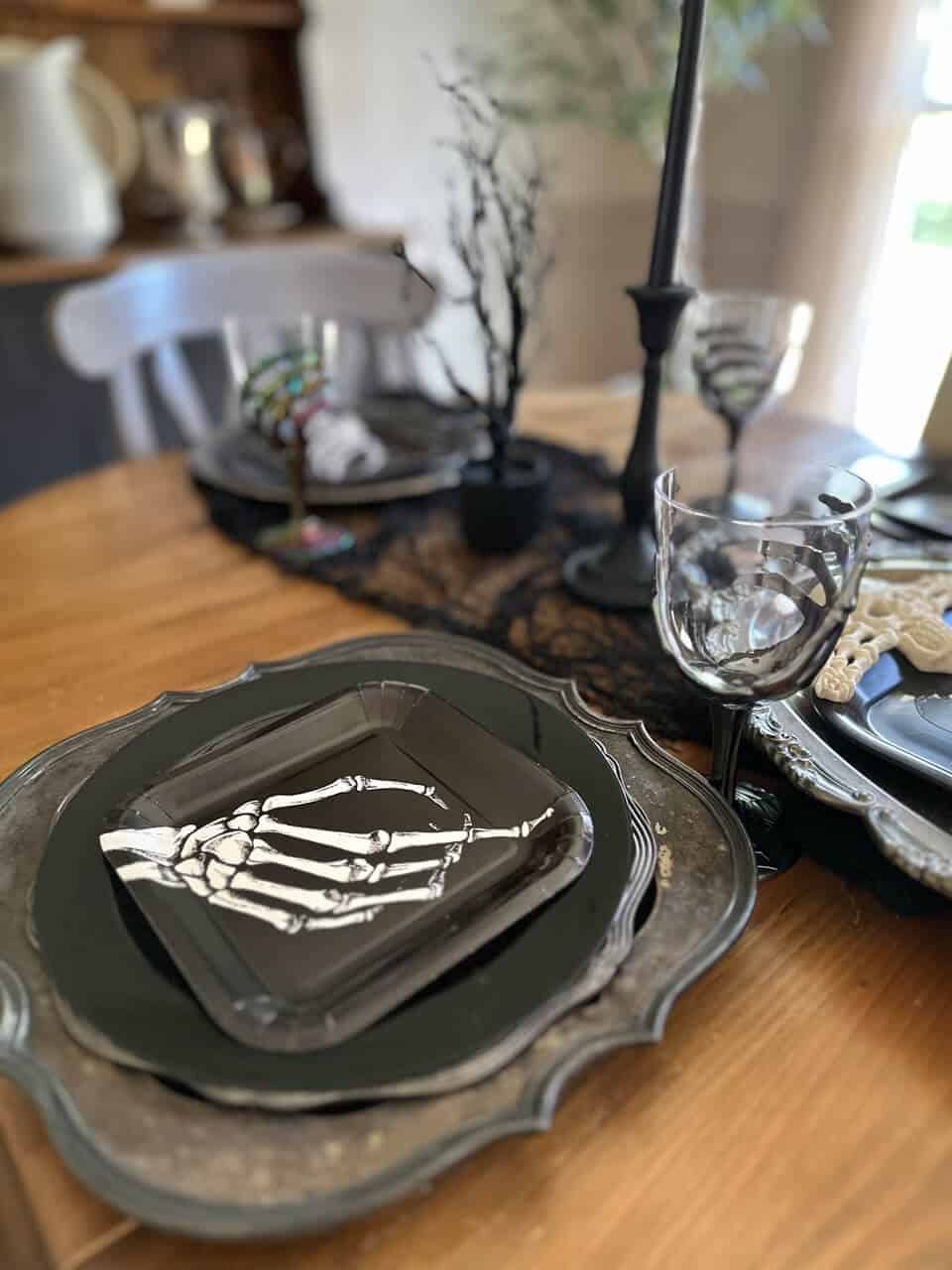 Halloween table setting with tarnished silver trays as chargers, black plated with skeleton hand square plates on top