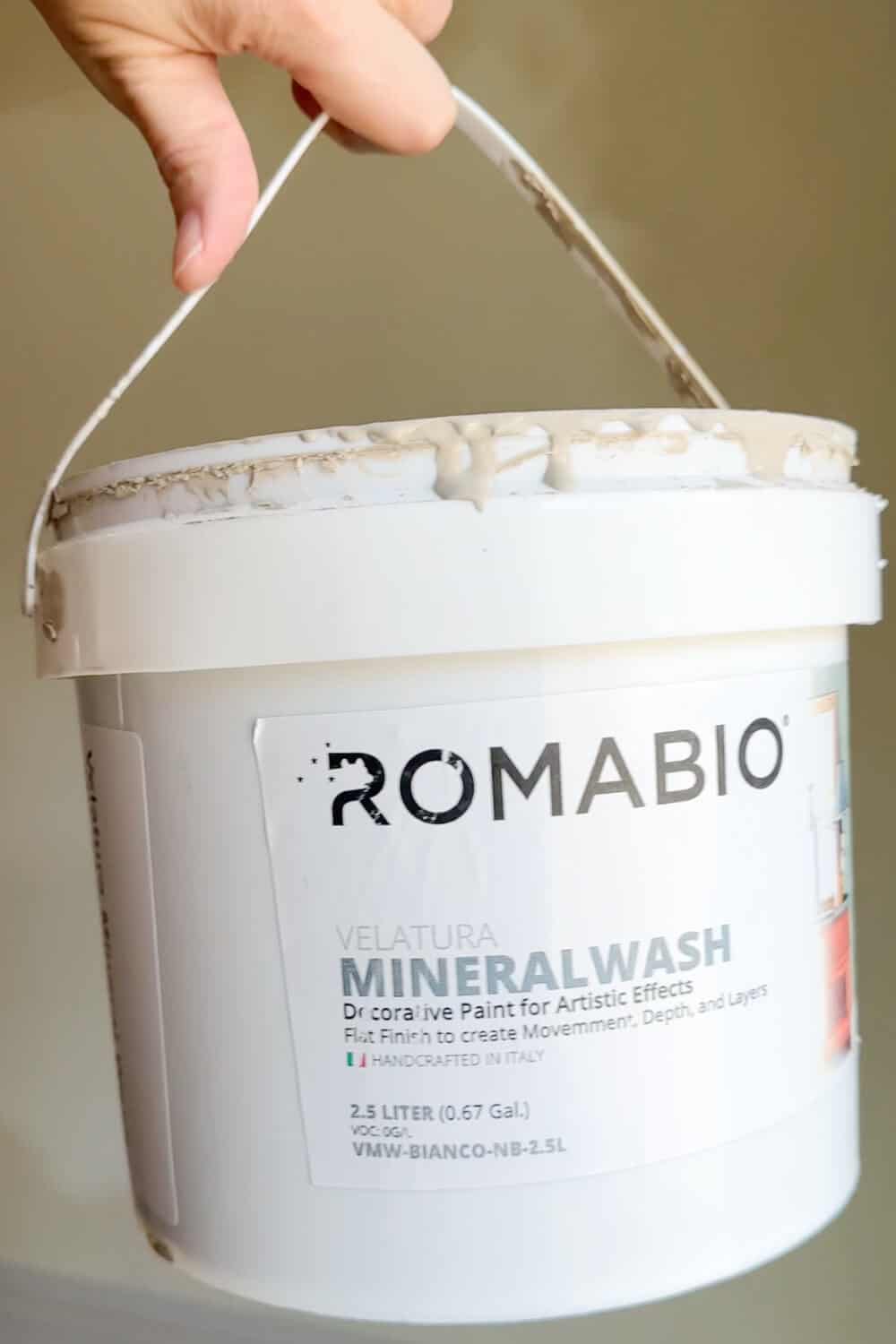 Open bucket of Romabio Velatura Mineralwash held in front of a limewashed wall