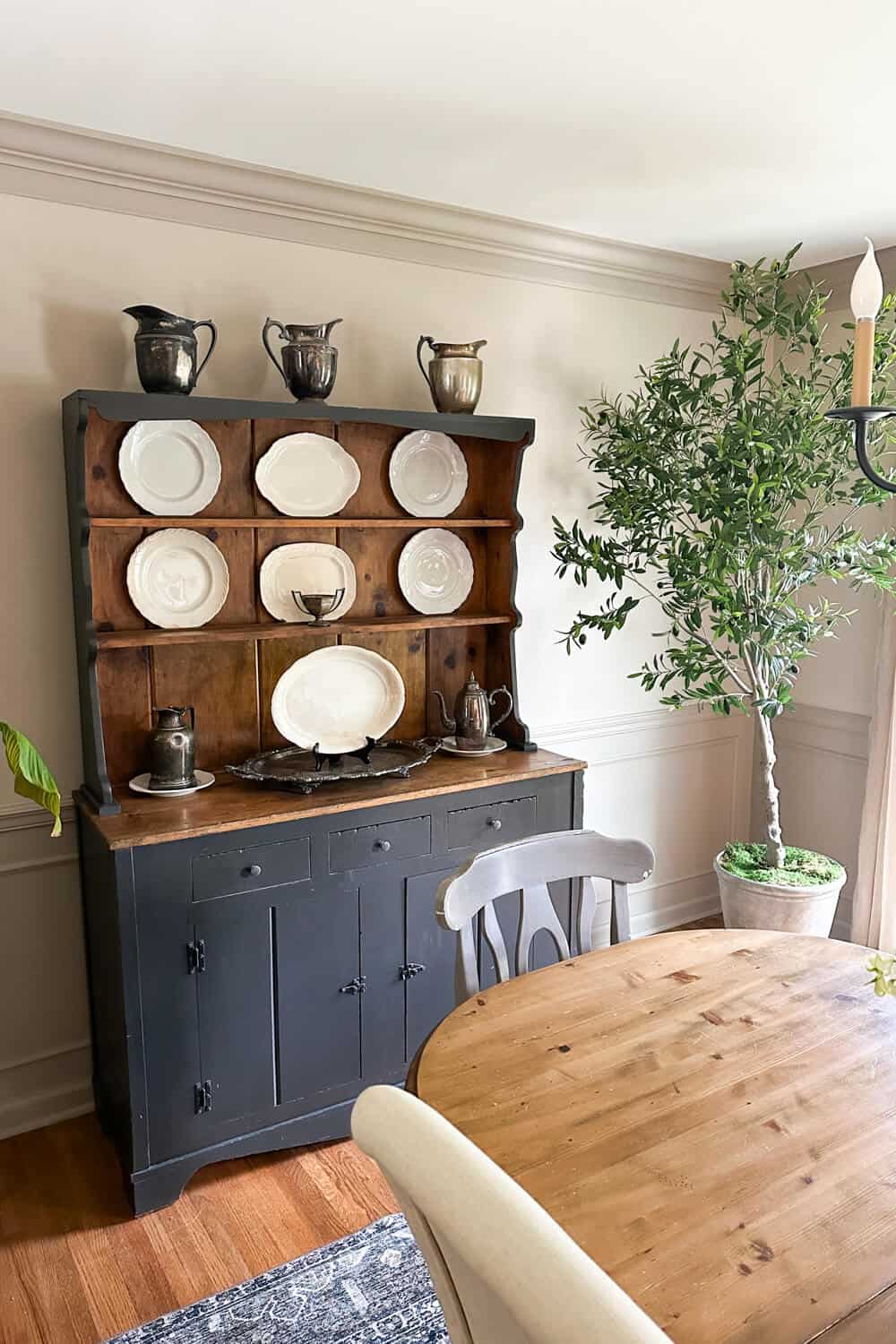 vintage hutch with ironstone plates and old silver in front of a limewashed wall with an olive tree in the corner