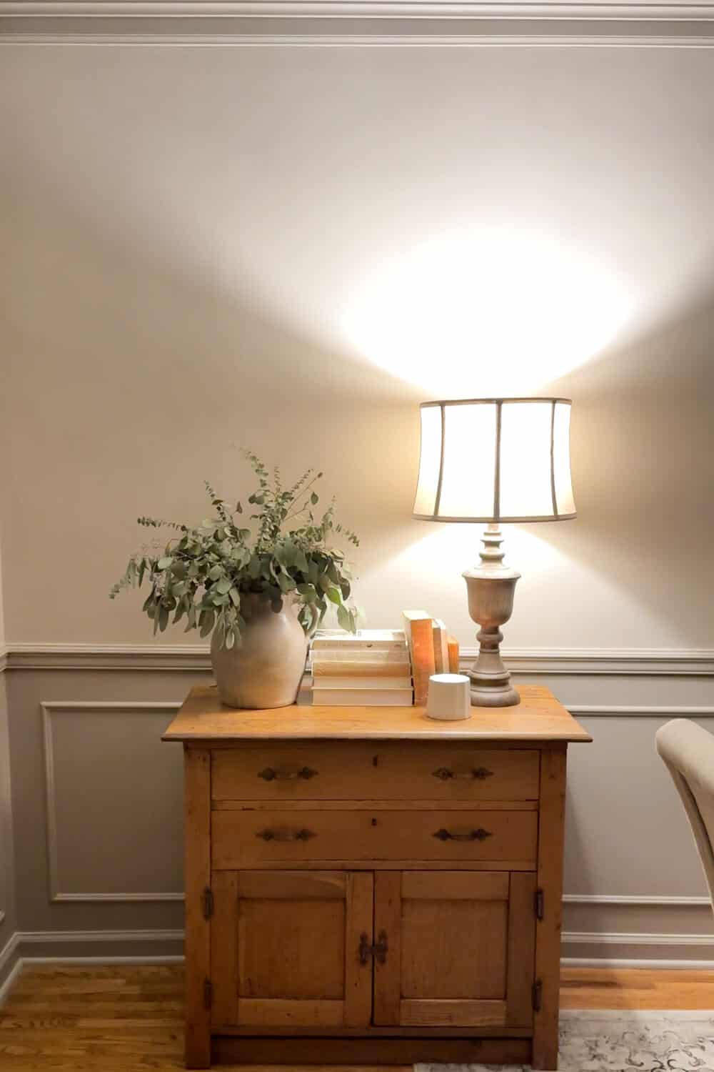 limewashed wall in the evening with a lamp on a chest with a vase of dried eucalyptus