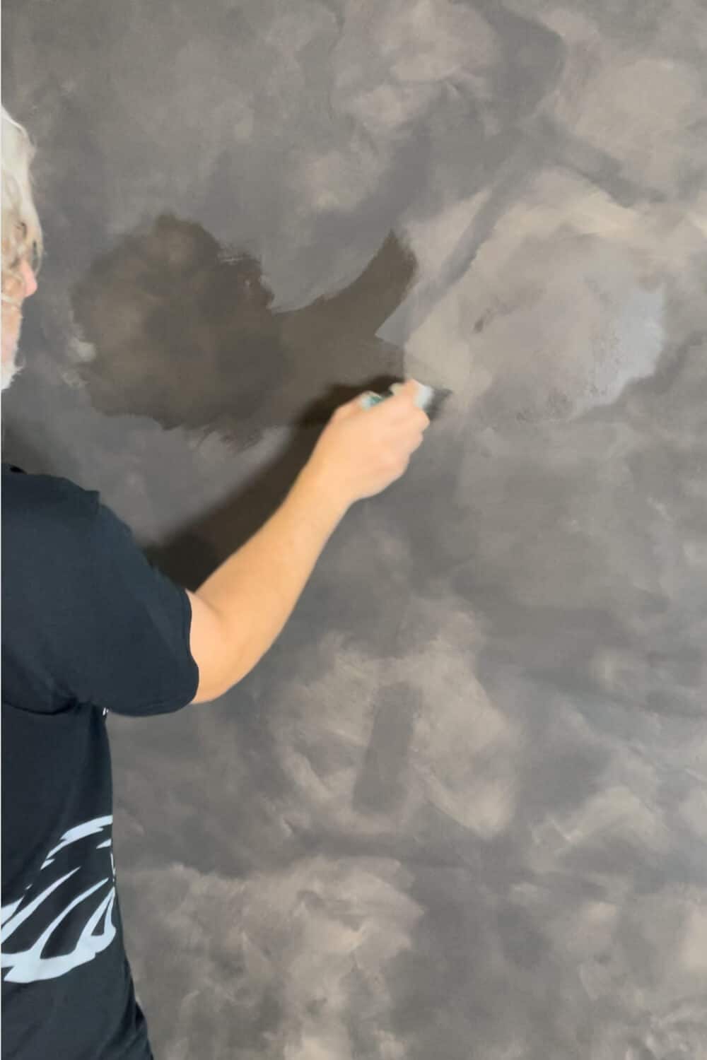 black wall being limewashed by man with gray hair
